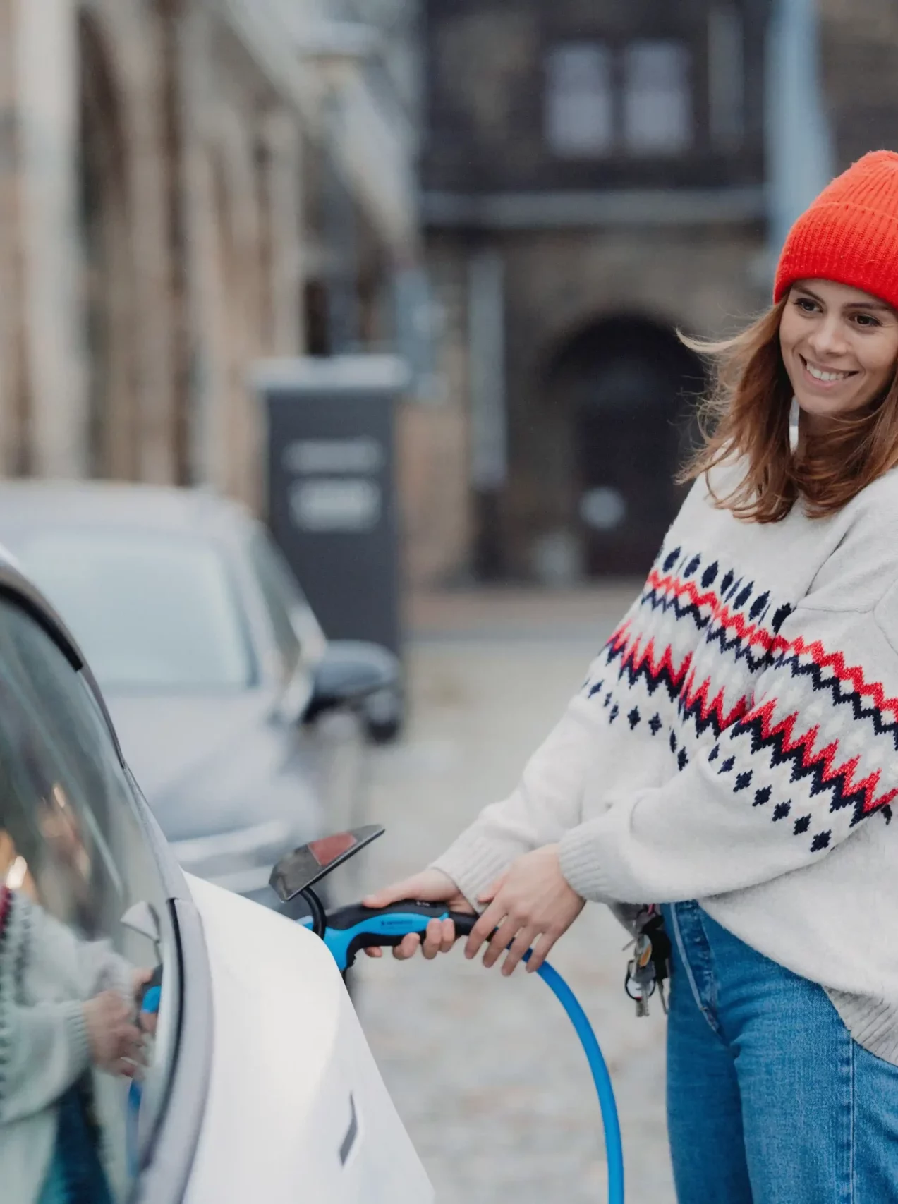 Lachende Frau mit roter Mütze beim Laden ihres Elektrofahrzeuges.